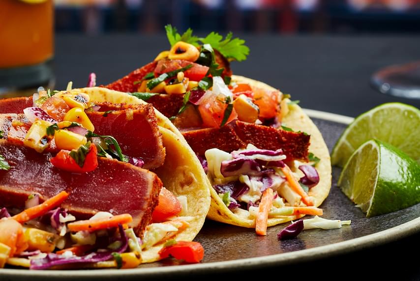 Closeup of a dish featuring FIREBAR Tuna Street Tacos alongside two slices of lime.